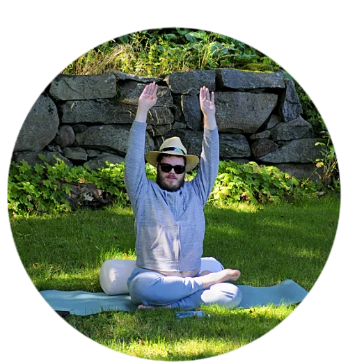 En person i solglasögon sitter på en gräsmatta och sträcker händerna uppåt.