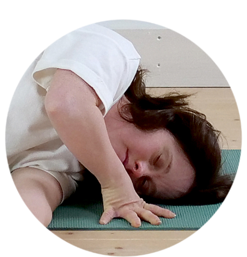 En person i vit t-shirt ligger på en yogamatta. Hon blundar.